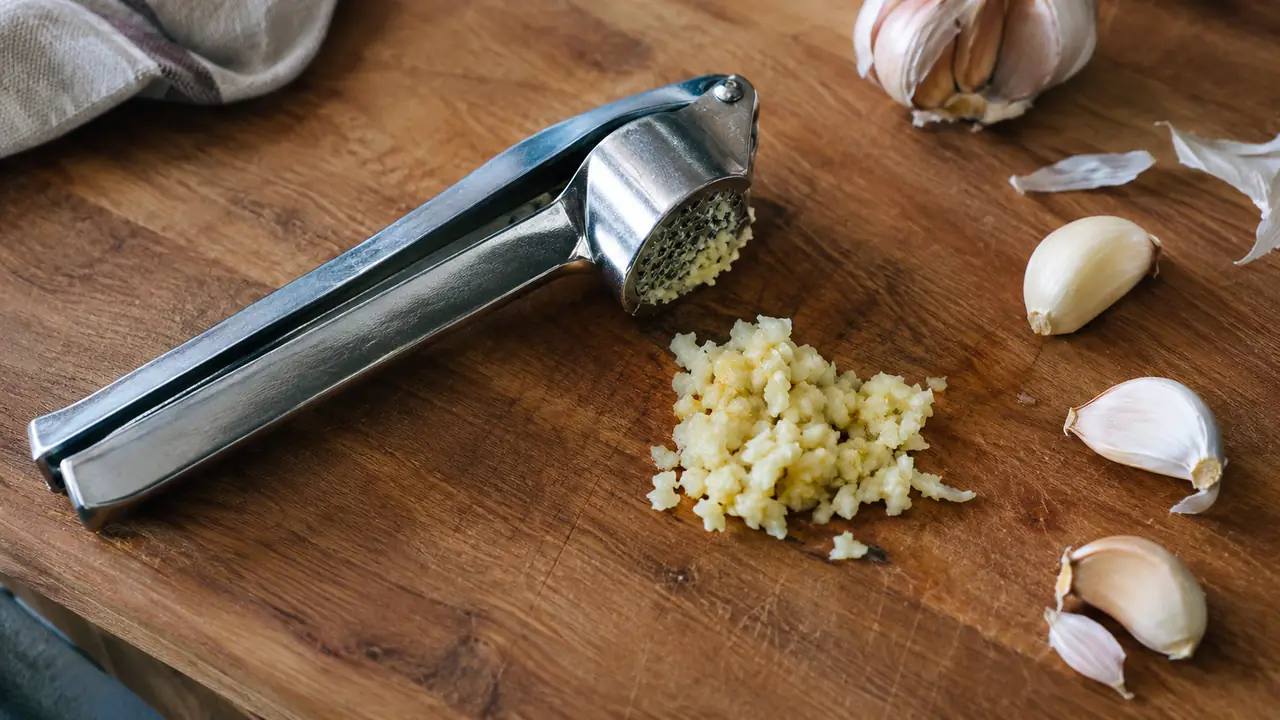 A simple illustration of a garlic press with a pile of minced garlic next to it on a cutting board